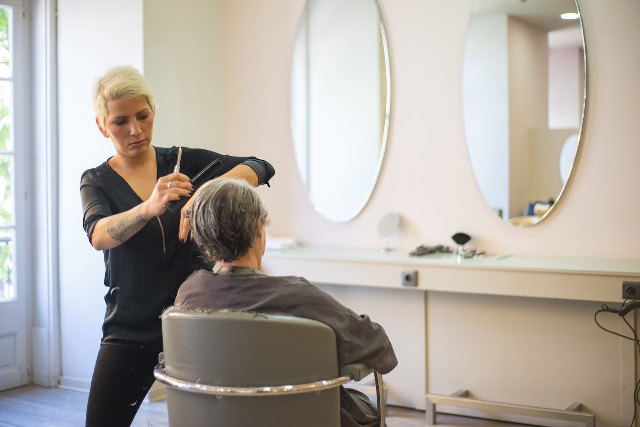 about-02 A hairdresser skillfully cuts an elderly woman's hair in a modern salon with mirrors and a comfortable barber chair.